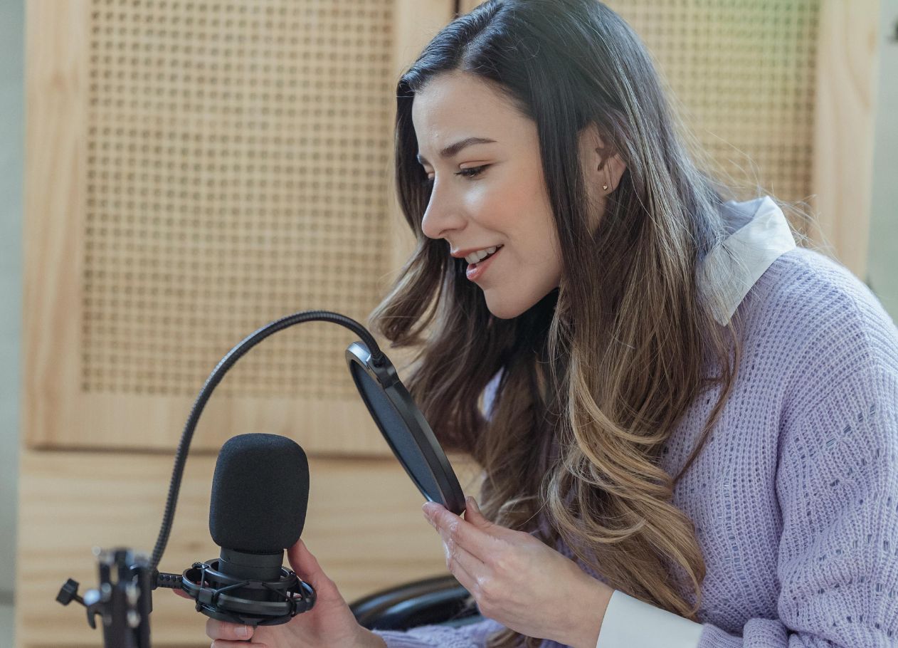 woman talking into a microphone for a podcast with wicker furniture behind her