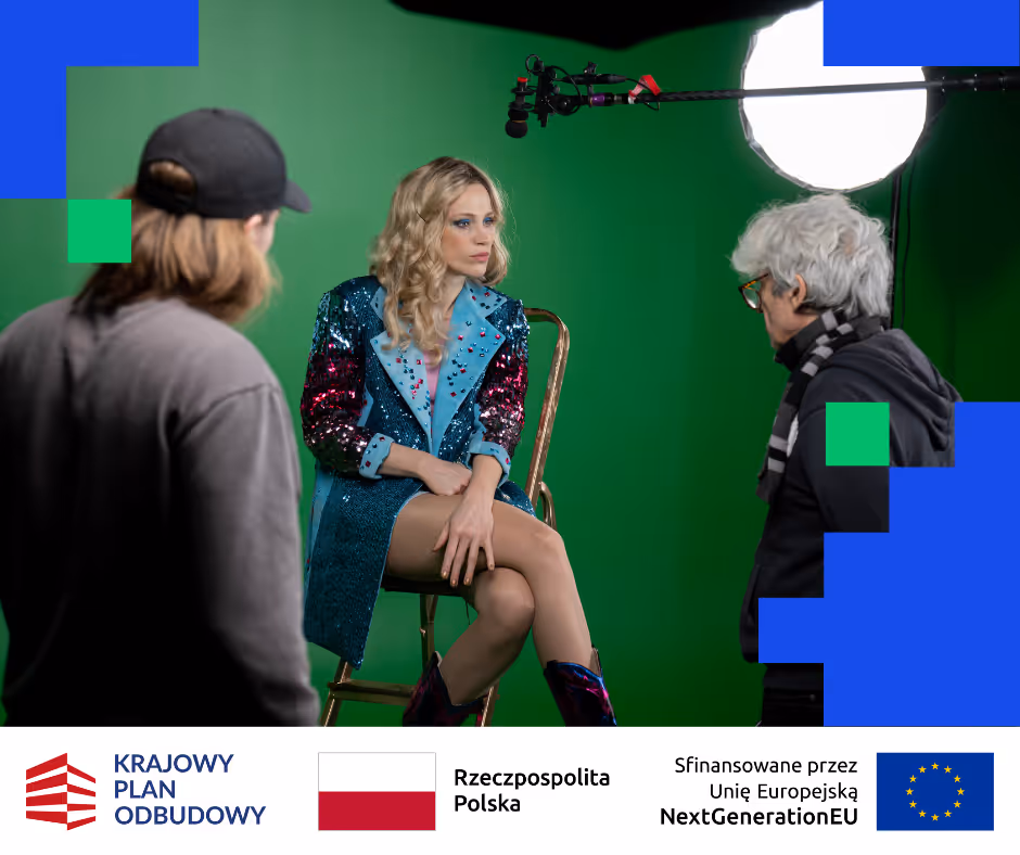 Kobieta w błyszczącym kostiumie siedzi na krześle przed zielonym ekranem, a dwie osoby rozmawiają z nią podczas nagrania.