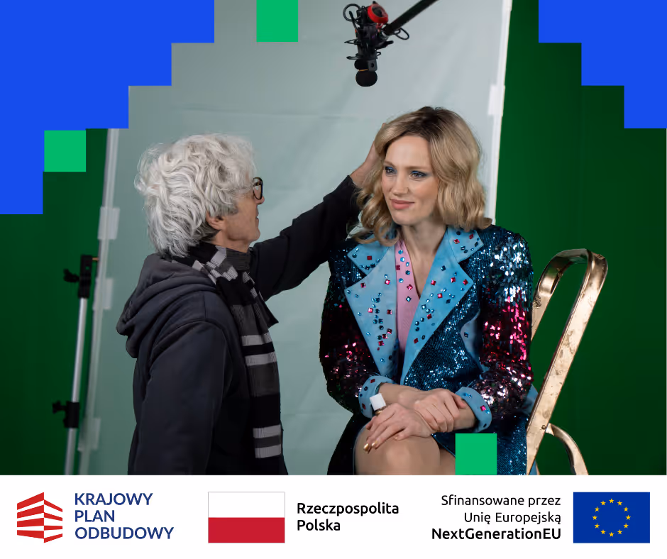 Kobieta w cekinowej marynarce siedzi na złotym krześle, podczas gdy starsza osoba z siwymi włosami i okularami poprawia jej fryzurę na planie filmowym z mikrofonem zawieszonym nad nimi.