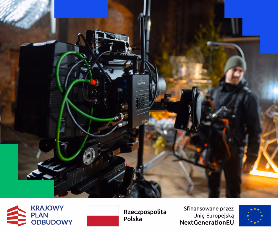 Profesjonalna kamera filmowa na statywie w centrum kadr, w tle operator kamery w ciemnym ubraniu i zielonej czapce.