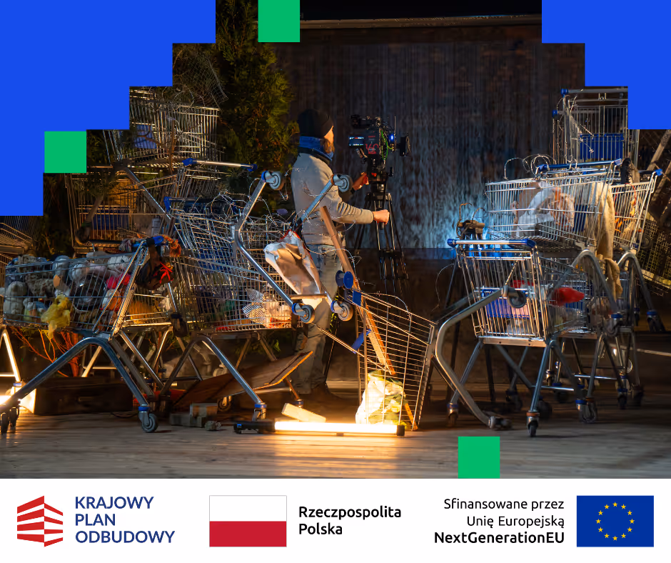 Osoba obsługująca kamerę filmową w otoczeniu porozrzucanych metalowych wózków sklepowych z materiałami i rekwizytami na scenie.