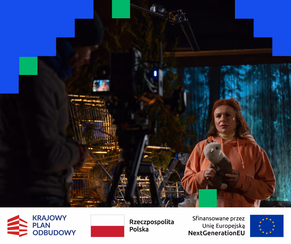 Kobieta w pomarańczowej bluzie trzyma pluszową zabawkę podczas nocnego nagrania filmowego z reżyserem i sprzętem w tle.