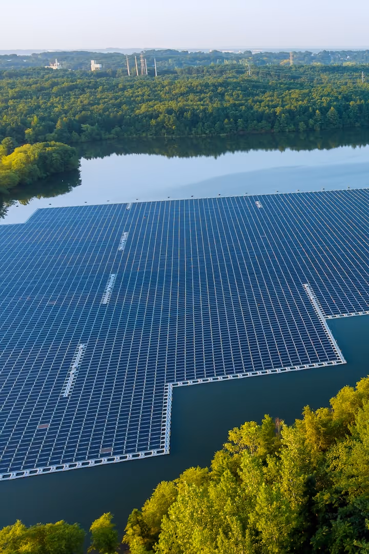 A large floating solar panel array on a calm body of water surrounded by dense green forest.