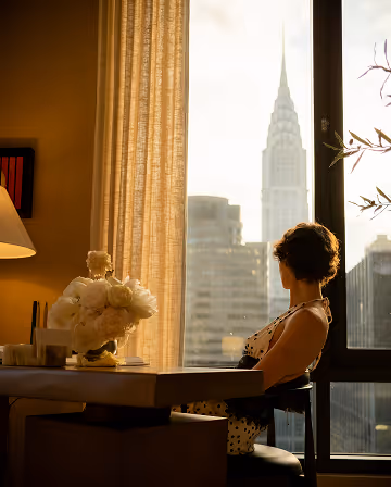 Woman sitting by a window overlooking the New York skyline, editorial photography for Monogram New York.