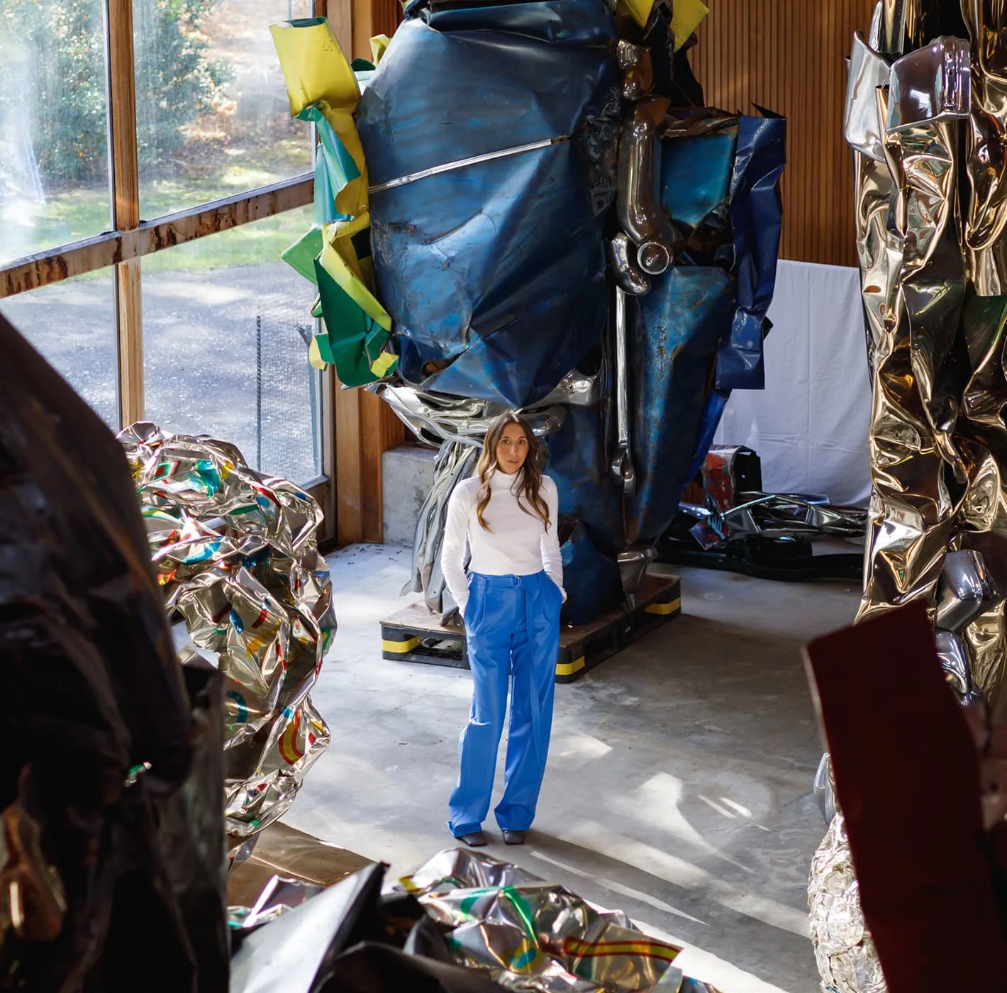 Woman standing among abstract metal sculptures in an art studio, editorial photography for Alexandra Fairweather.