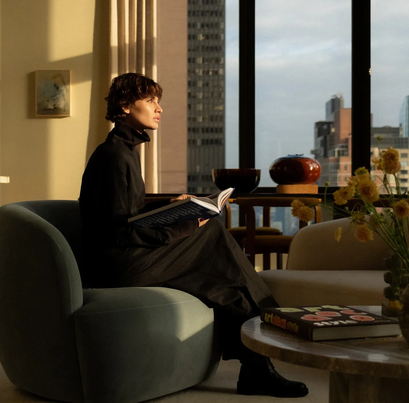 Woman reading a book in a modern apartment with city skyline view, editorial photography for Monogram New York.