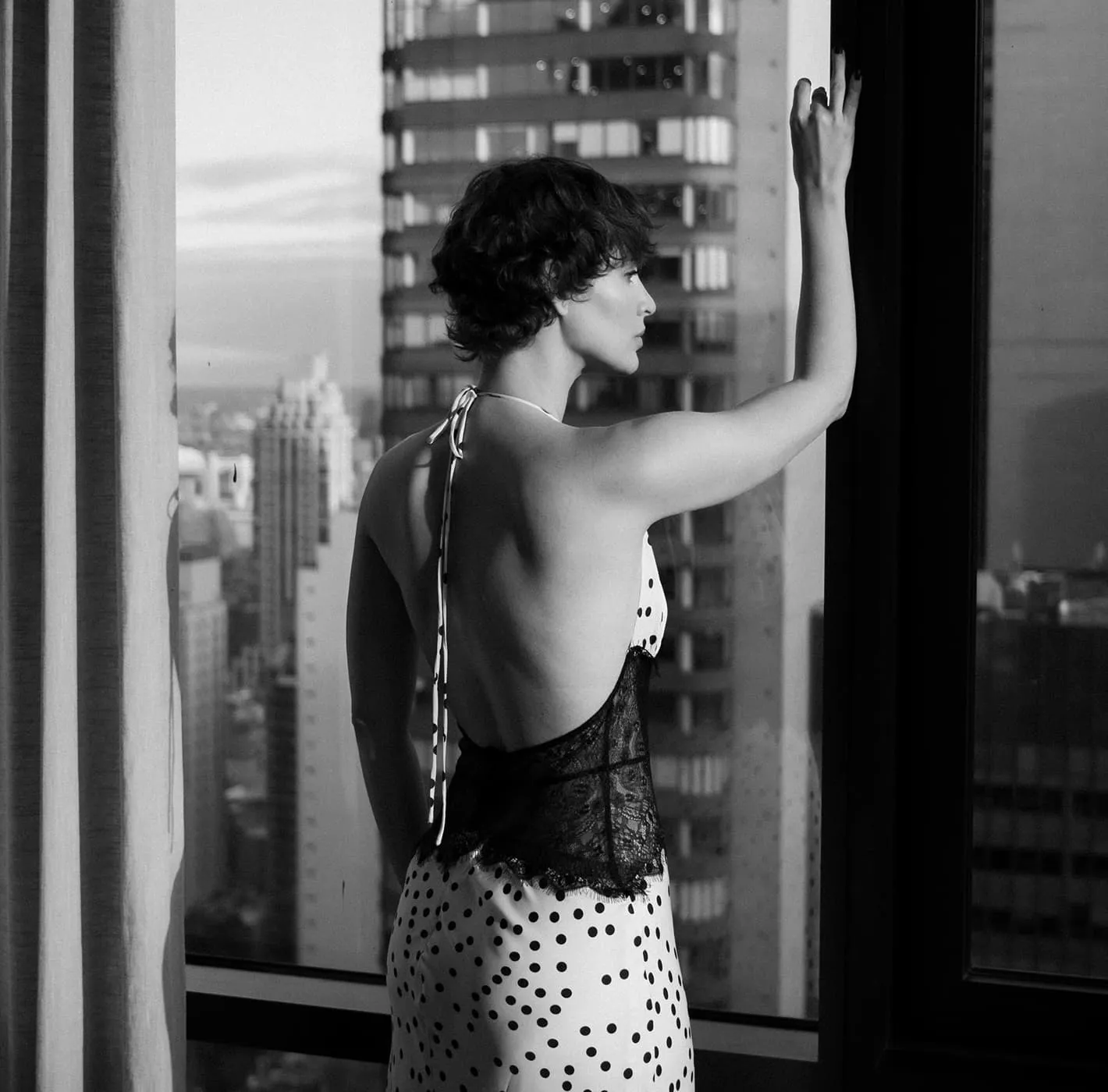 Black and white portrait of a woman standing by a window with New York skyline view, editorial photography for Monogram New York.