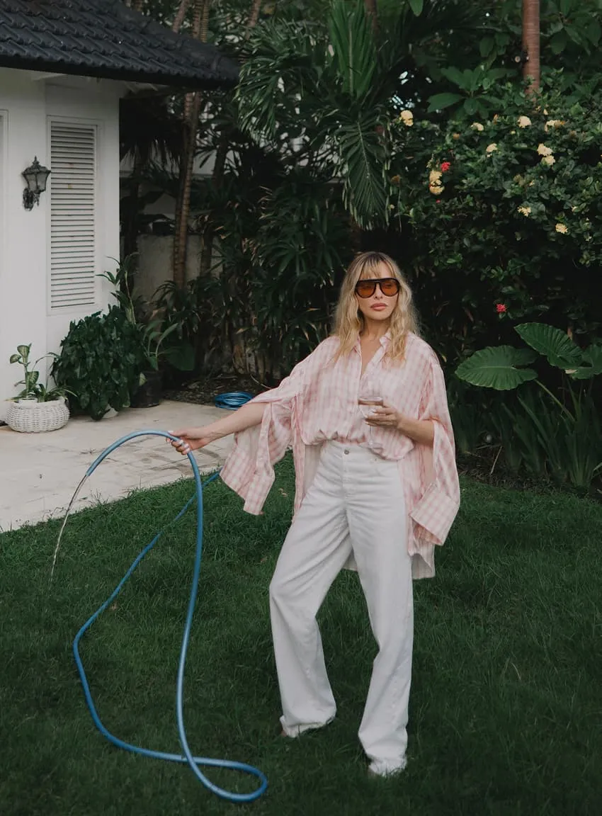 Woman standing in a tropical garden holding a garden hose, editorial photography for Natalya Pavchinskaya.