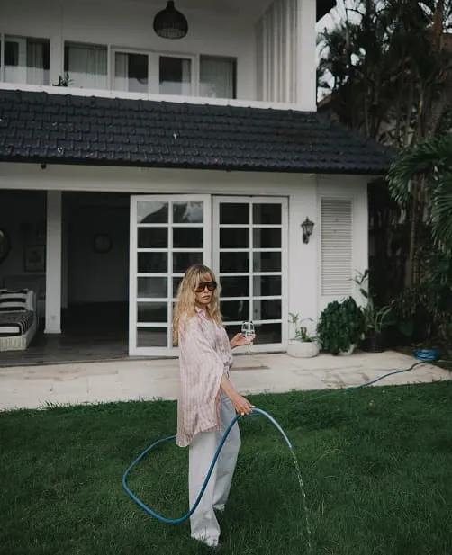 Woman watering the lawn in a tropical garden, editorial lifestyle photography for Natalya Pavchinskaya.
