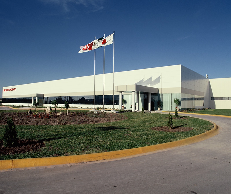 Planta Nippondenso de fachada blanca, con banderas de México y Japón.
