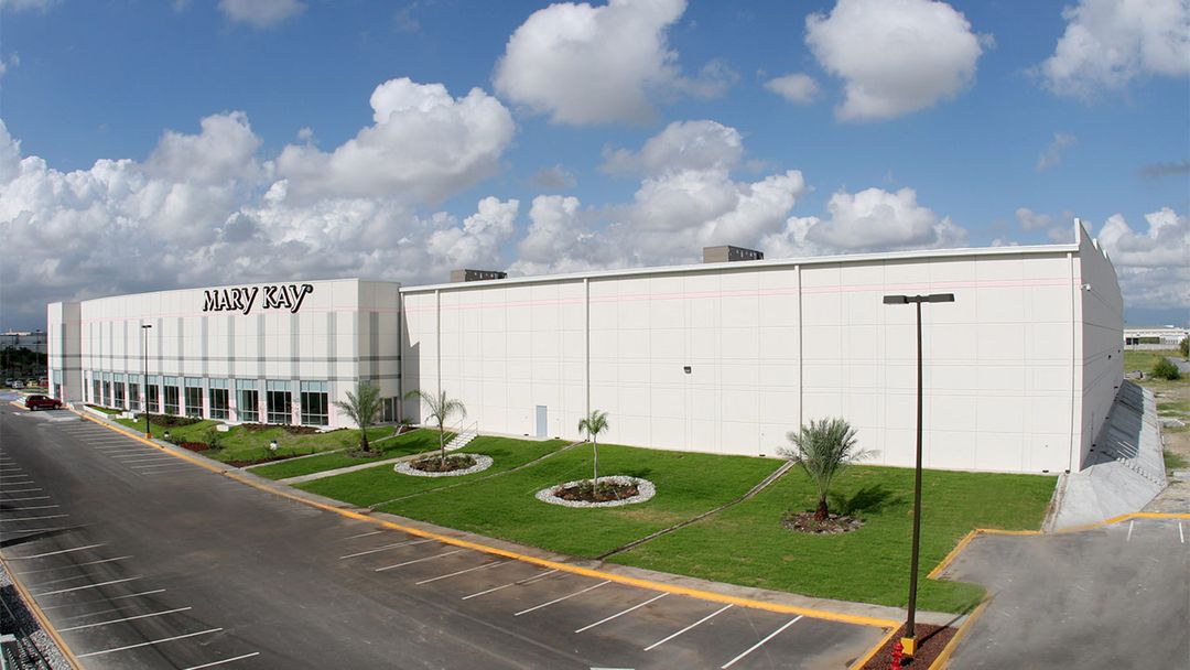 Planta Mary Kay de volumen blanco, con palmeras y jardines al frente.