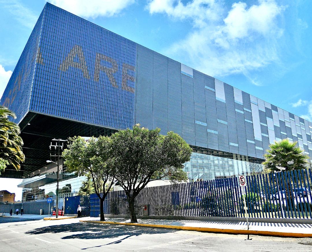 Fachada de cristal azul de la Arena Ciudad de México, con letras doradas.