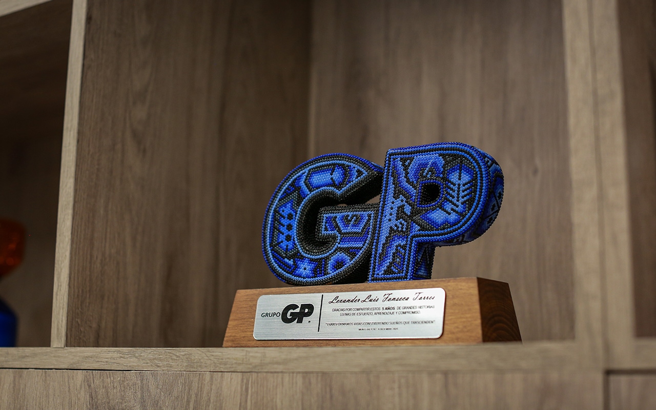 Escultura de chaquiras con las letras GP y placa de Grupo GP en un estante.