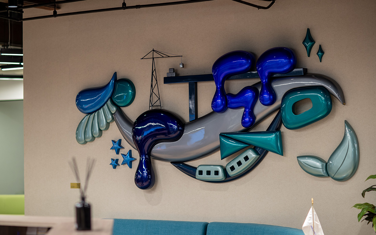 Mural escultórico de las letras GP, con grúa, estrellas y hojas en la oficina.
