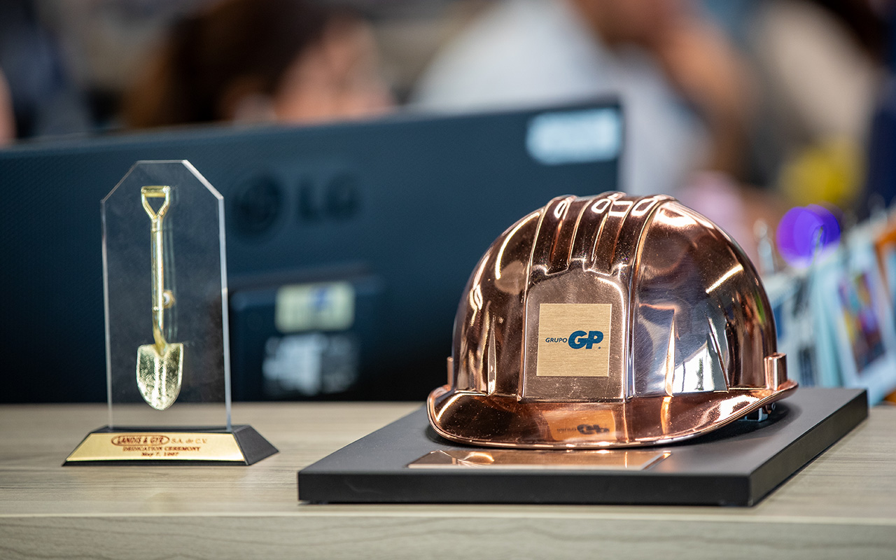 Casco metálico de GP junto a un trofeo de pala dorada sobre un escritorio.