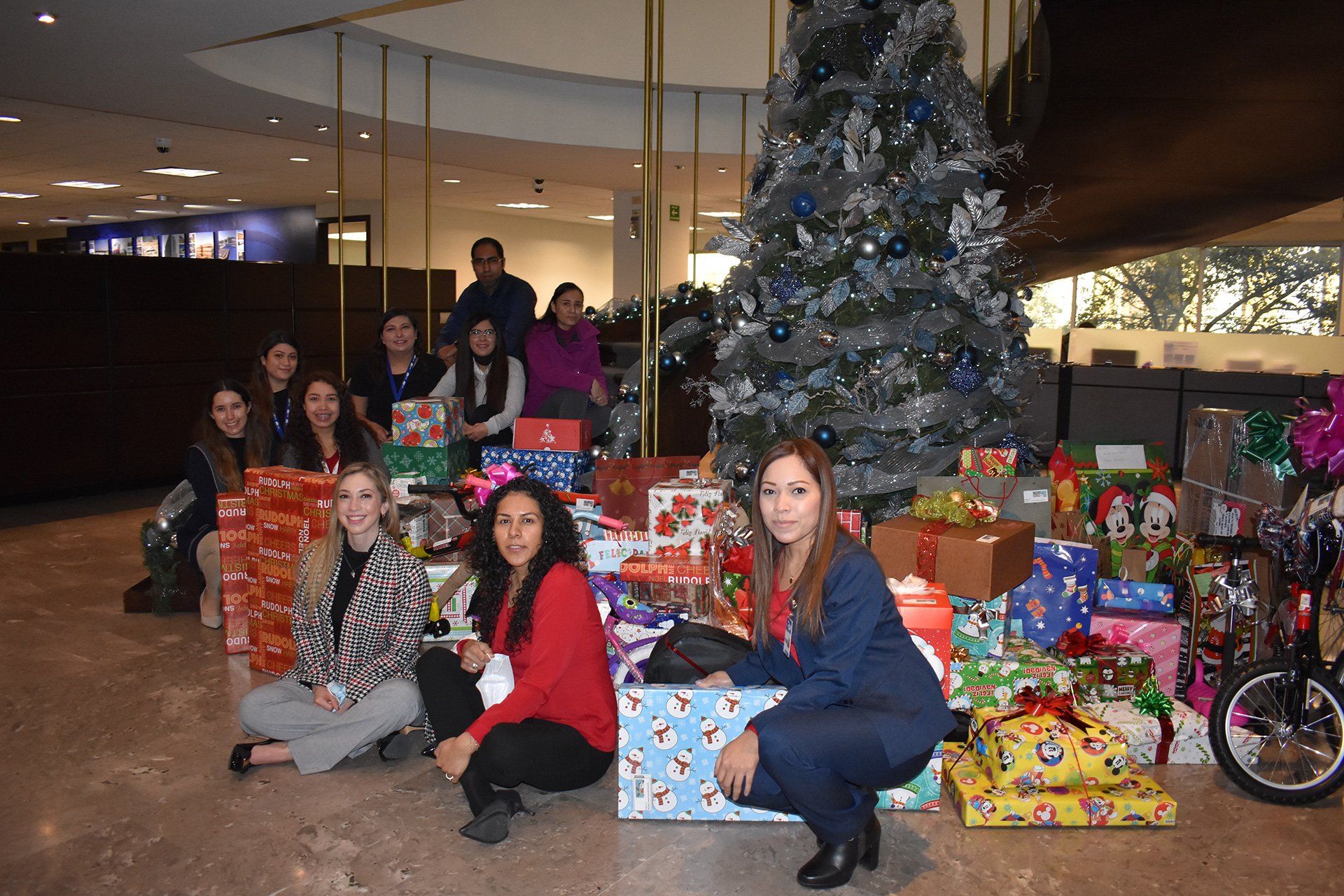 Employees pose with Christmas gifts next to a decorated tree in the office.