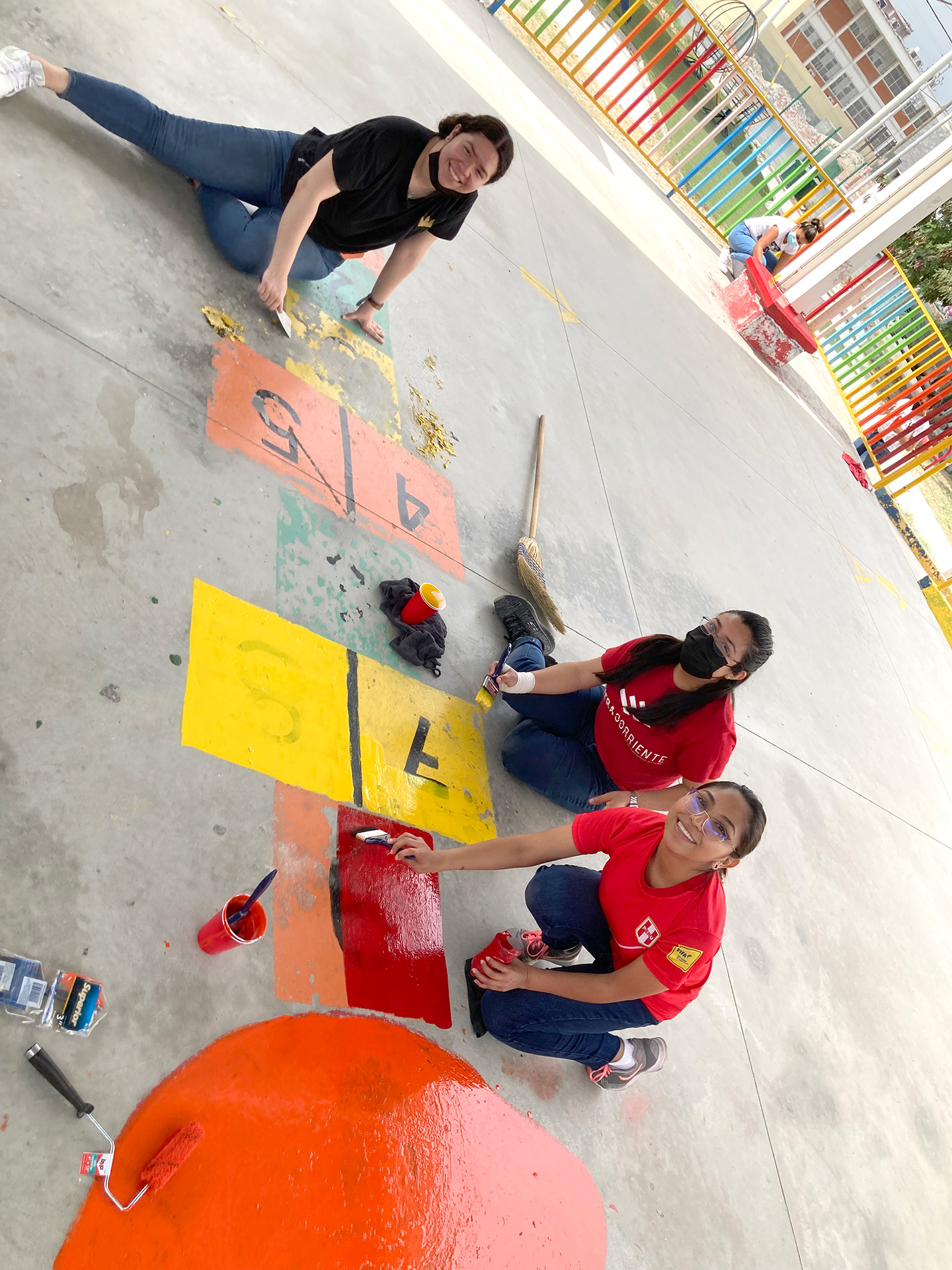 Volunteers are painting a colorful airplane set in a schoolyard.