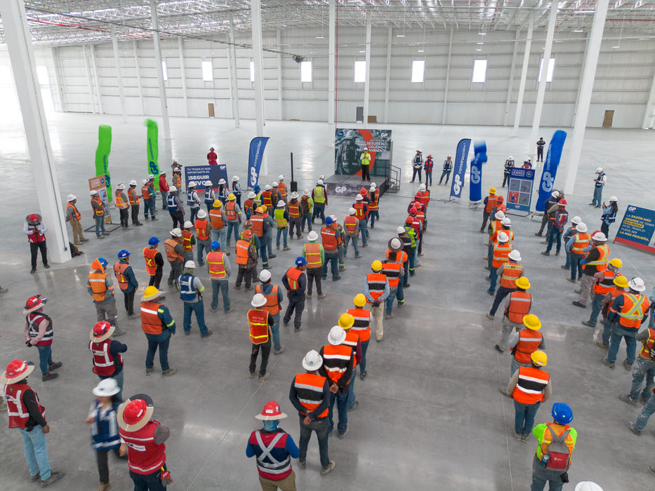 Vista aérea de trabajadores en círculo dentro de una nave, con banderas de GP.