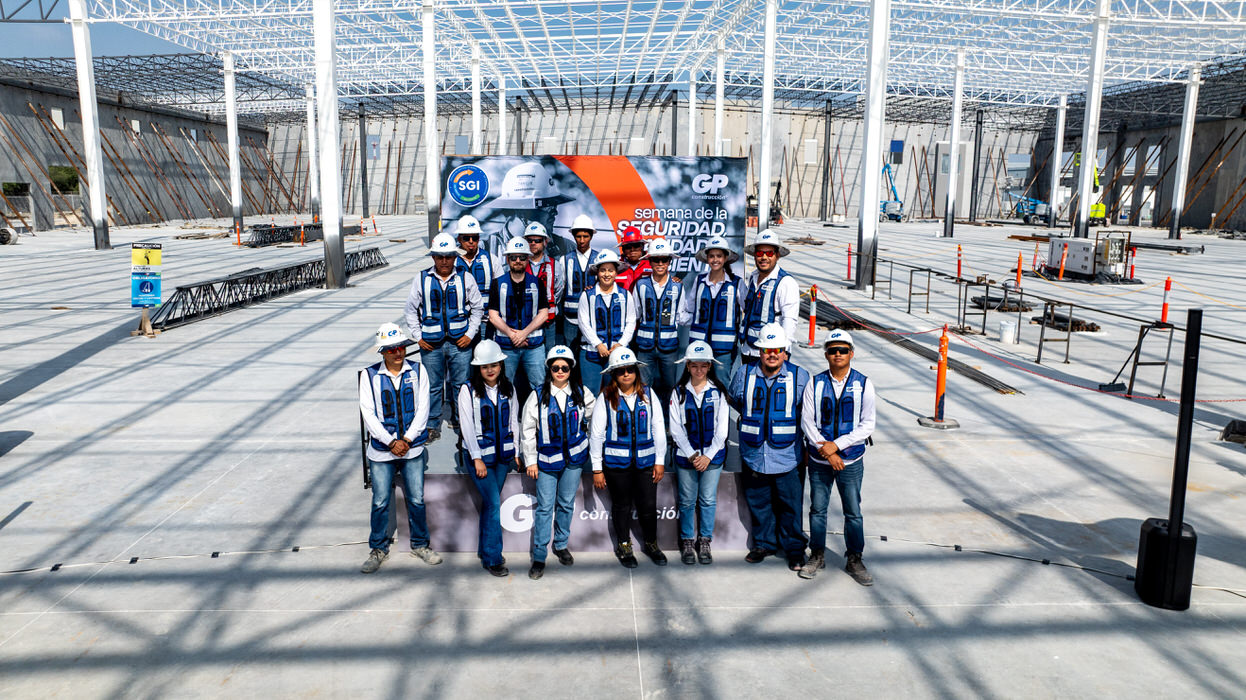 Grupo con chaleco azul posa bajo la estructura de acero, frente al letrero de GP.