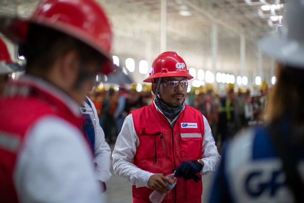 Supervisor con casco y chaleco rojo conversa entre compañeros dentro de la nave.