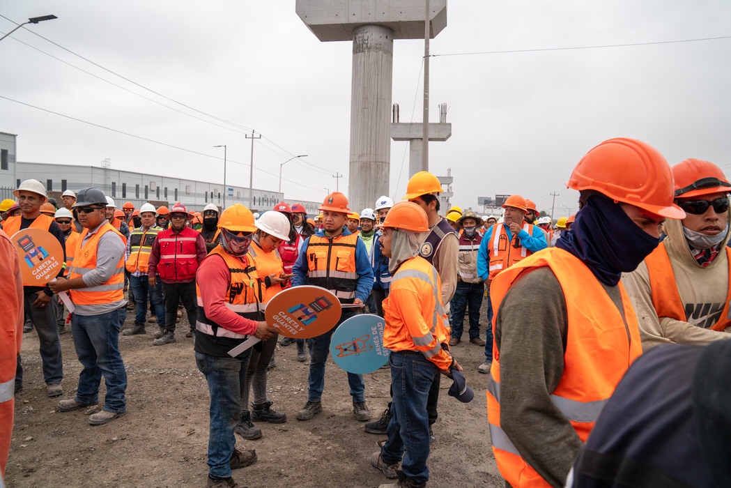 Trabajadores con chaleco naranja sostienen reconocimientos circulares junto a una columna.