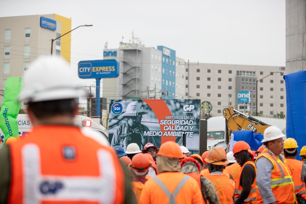 Cuadrilla de espaldas escucha frente al letrero de la Semana de la Seguridad, en exterior.
