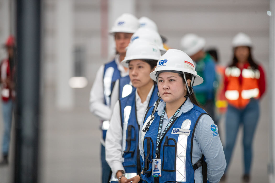 Mujeres con casco blanco y chaleco azul de GP escuchan de pie en la nave.