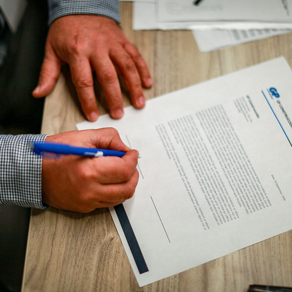 Manos firman un documento con membrete de GP Construcción sobre el escritorio.