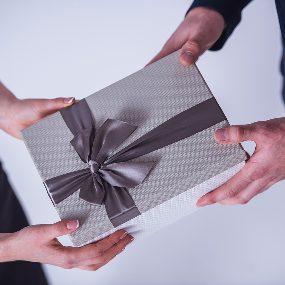 Dos personas intercambian una caja de regalo gris con listón.