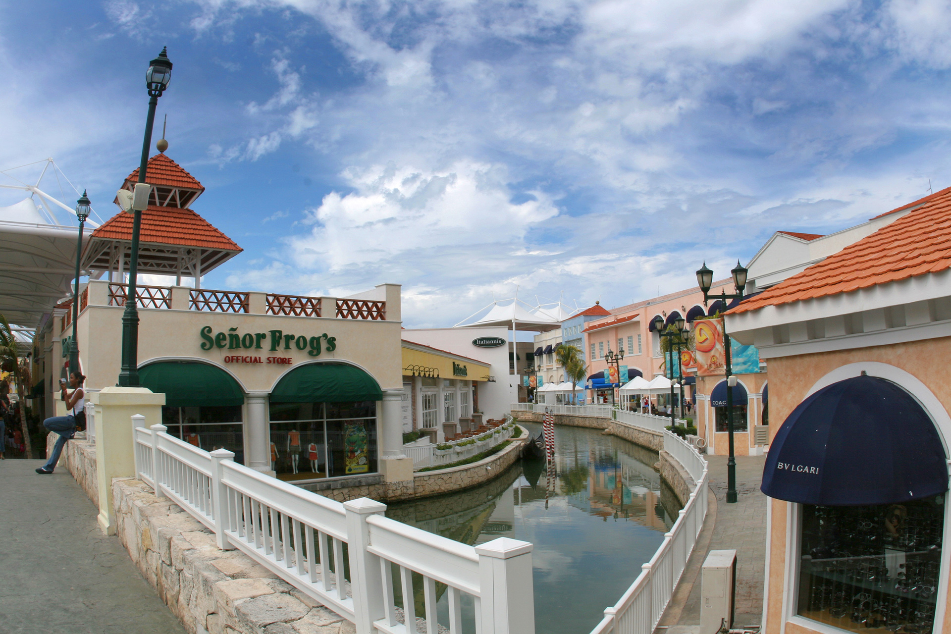 Plaza comercial con canal, locales y el anuncio de Señor Frog's, bajo nubes.