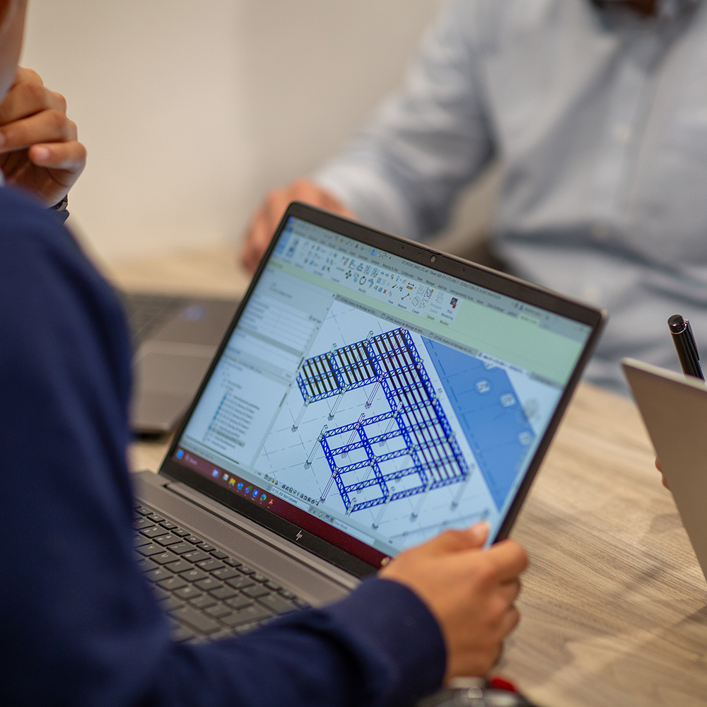 Equipo revisa un plano estructural azul en una laptop durante una junta.