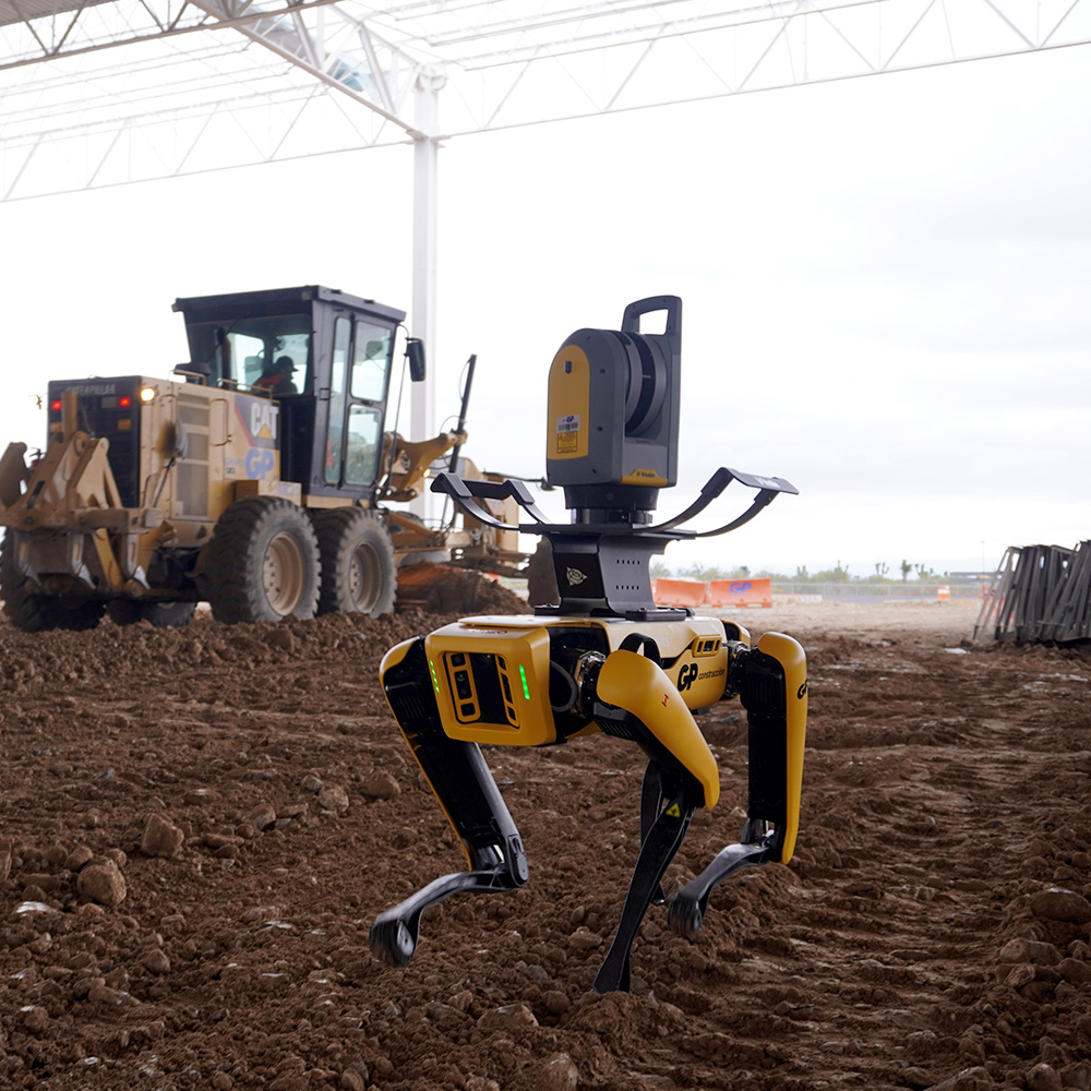 Robot cuadrúpedo con equipo de topografía en un terreno de obra, junto a maquinaria.