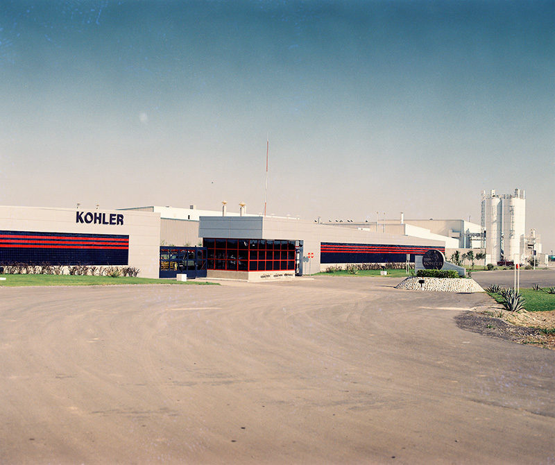 Fachada de la planta Kohler, con franjas rojas, silos y acceso vehicular.