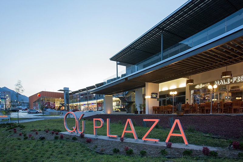 Letras luminosas de Qú Plaza al anochecer, frente a una terraza.