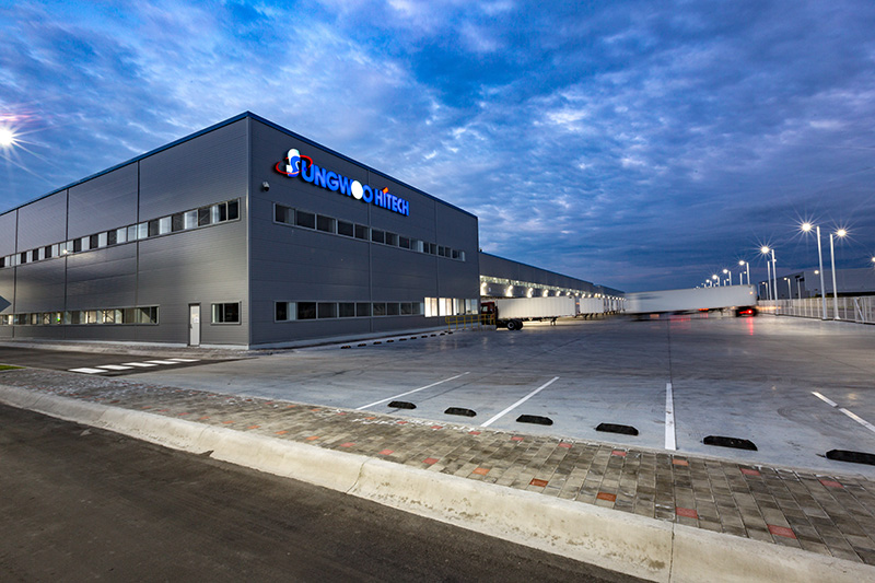 Fachada de Sungwoo Hitech al anochecer, con el logotipo iluminado.
