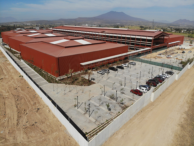 Vista aérea de las naves rojas de Betterware, con estacionamiento y un cerro.
