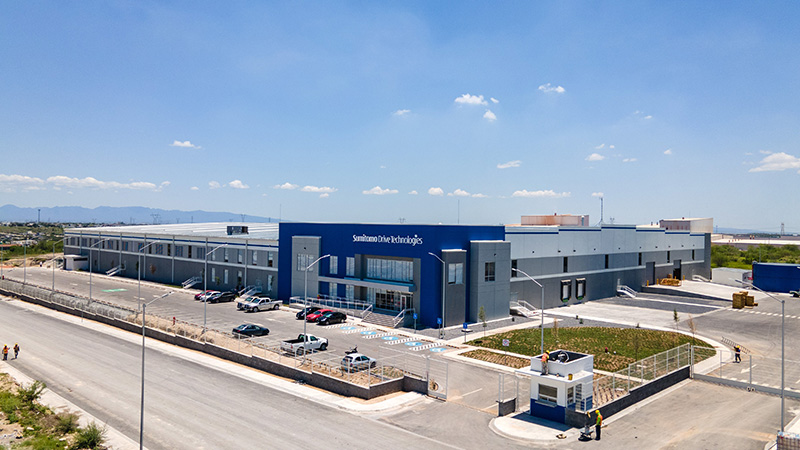Planta de Sumitomo Electric, con fachada azul y caseta de vigilancia.