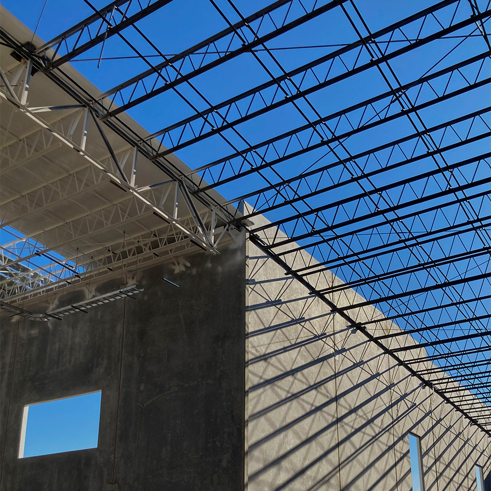 Armadura metálica y muro de concreto de una nave, contra el cielo azul.