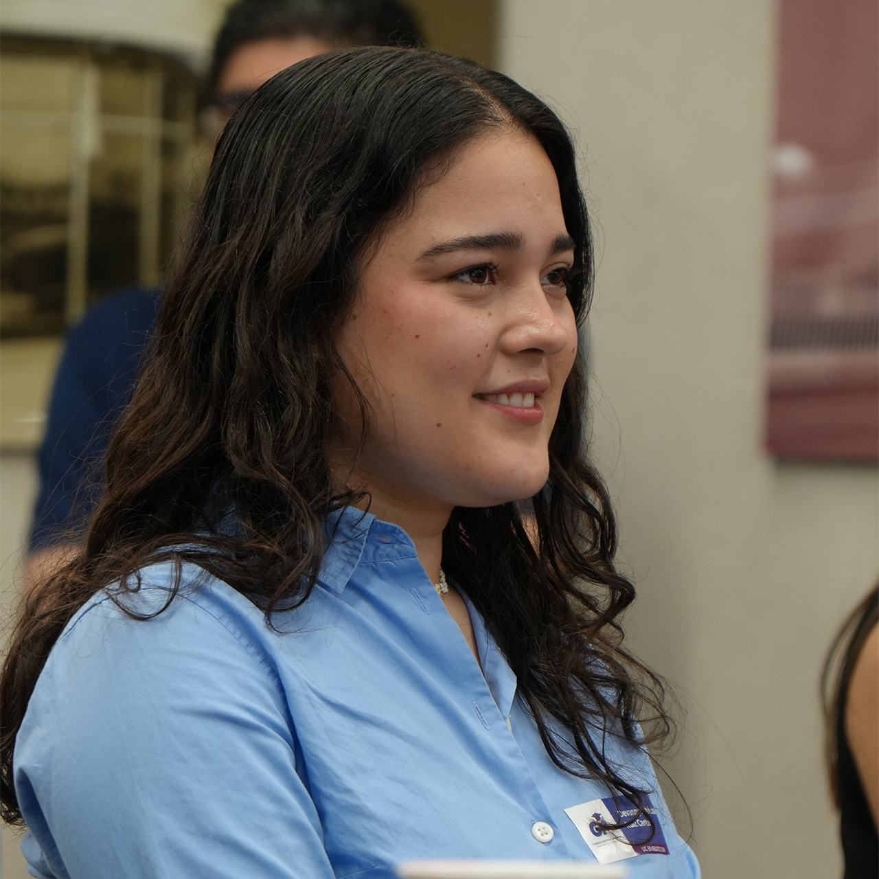 Joven con blusa azul y gafete sonríe durante un evento de la fundación.