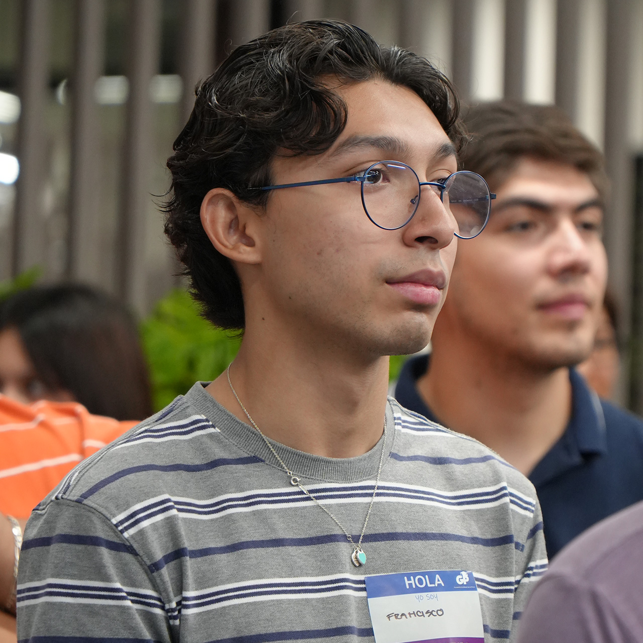 Joven con lentes y gafete escucha atento en un evento de la fundación.