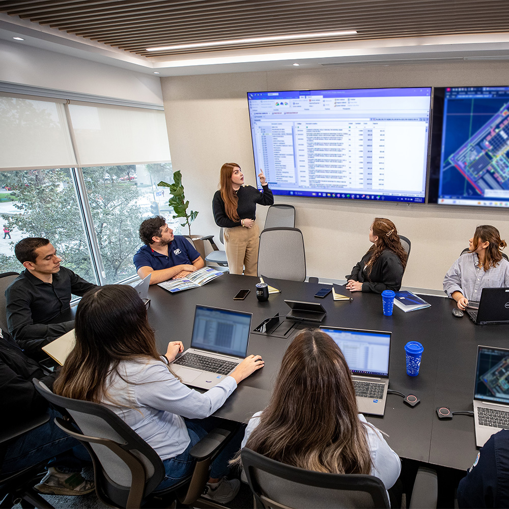 Equipo en sala de juntas revisa un programa de obra en pantallas y computadoras.