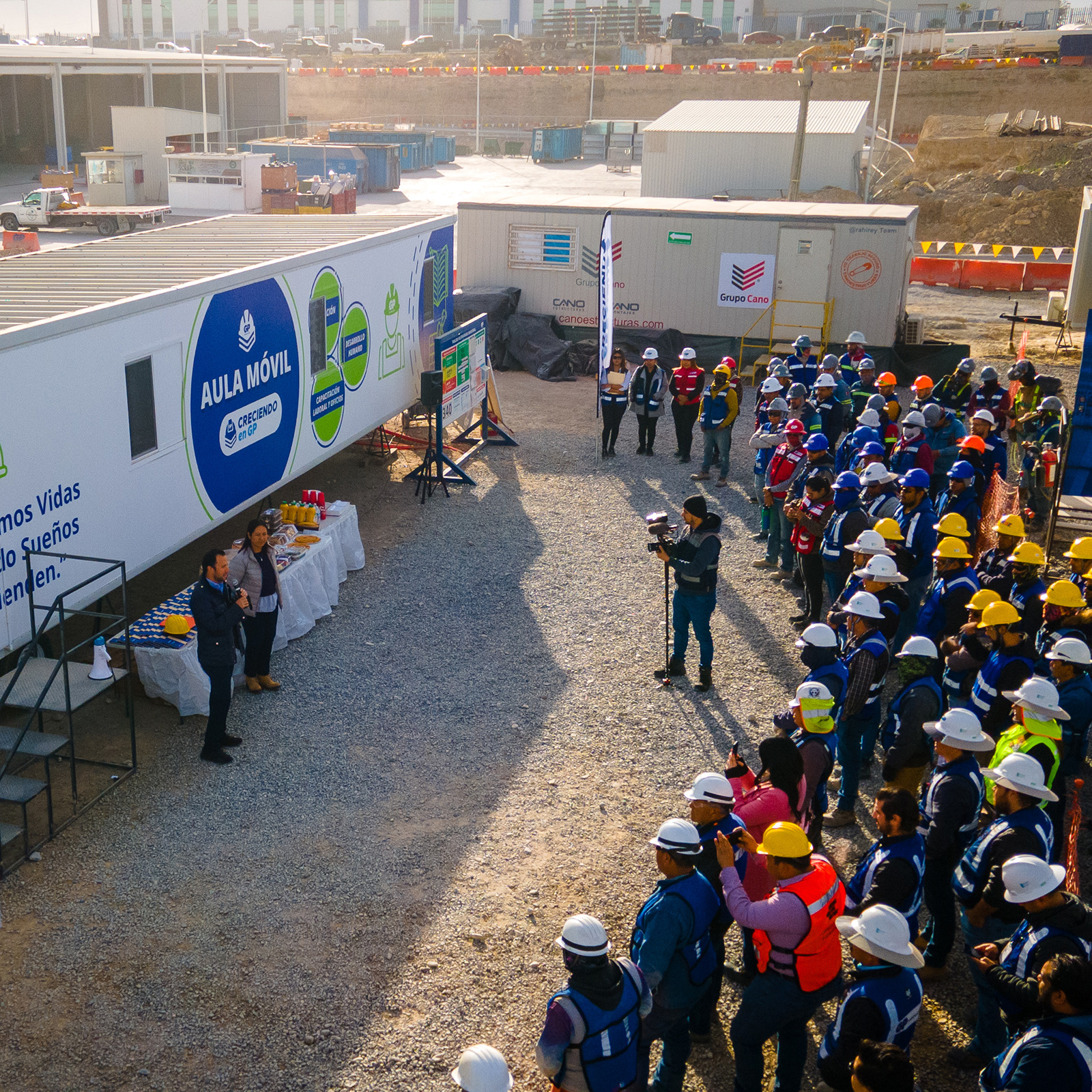 Cuadrilla con casco reunida frente al aula móvil en un patio de obra.