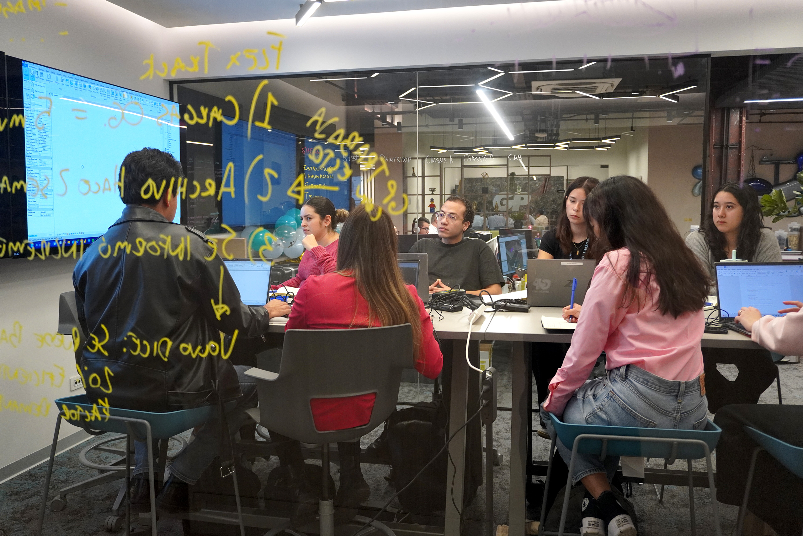Alumnos de Academia GP en computadoras, junto a un vidrio con notas amarillas.