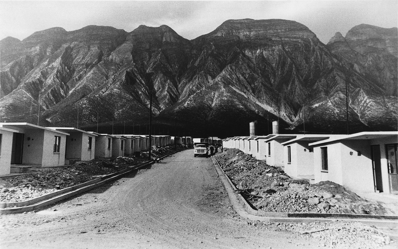 Casas de una planta en hilera al pie de la sierra, en toma histórica en blanco y negro.