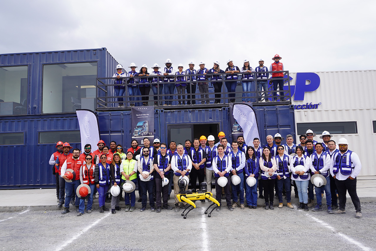 Equipo de GP posa frente a oficinas de contenedores, con un robot cuadrúpedo amarillo.