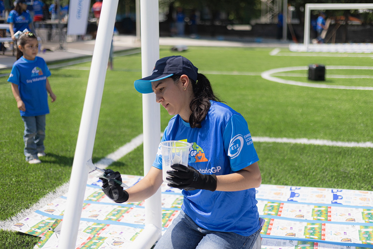 A volunteer from Grupo GP paints a white goal on a soccer field.