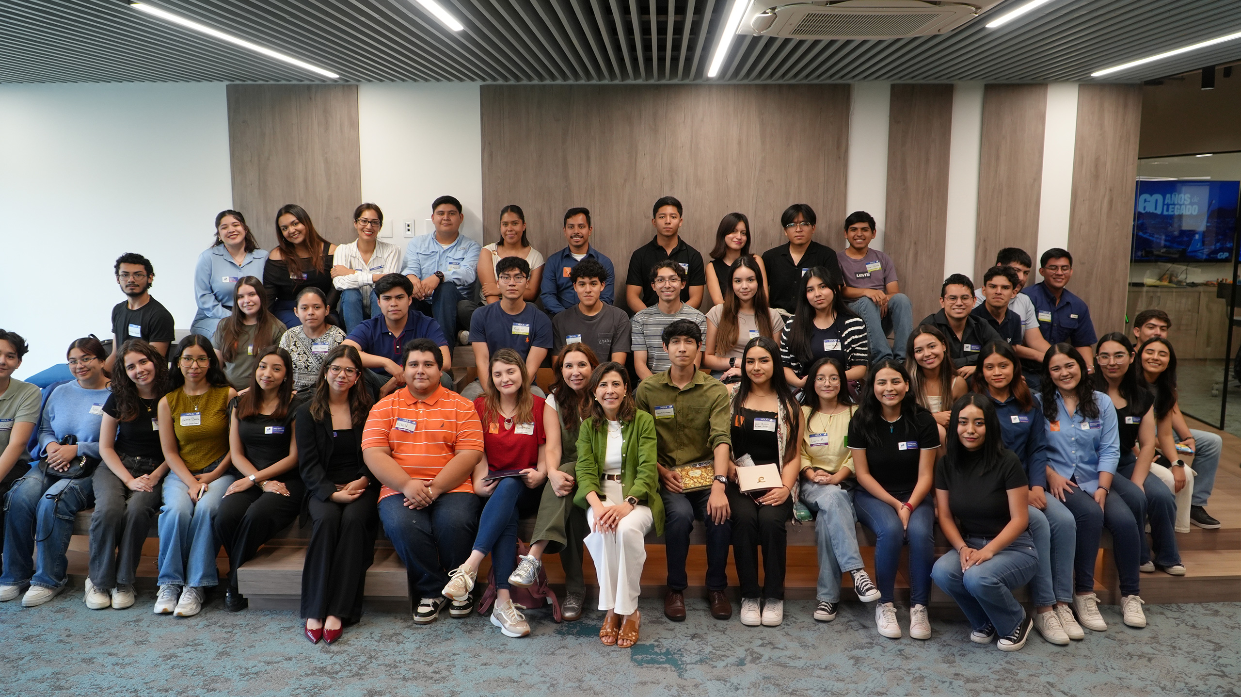 Grupo grande de jóvenes posa en filas en un salón con muro de madera.