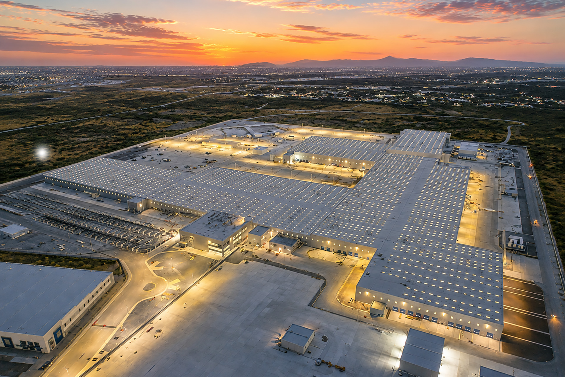 Parque industrial iluminado al atardecer, con naves, patios y cerros al fondo.