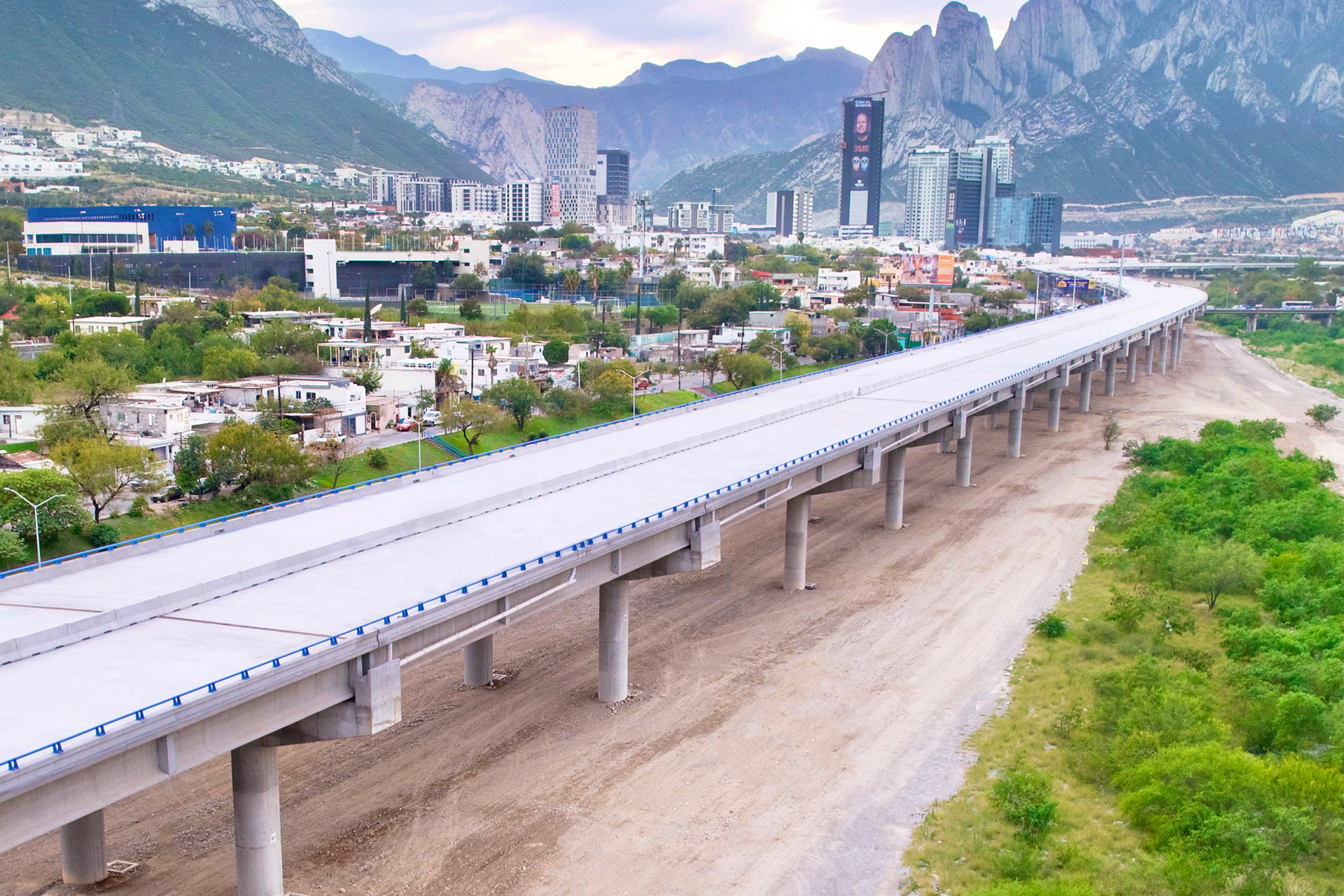 Viaducto elevado de concreto atraviesa la ciudad, con la sierra al fondo.