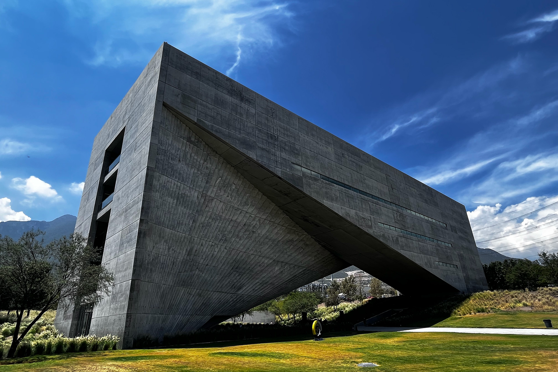 Fachada de concreto en voladizo, tomada desde el jardín contra un cielo intenso.